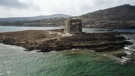 Aerial-backward-shot-of-the-medieval-Pelosa-watchtower-on-the-rocky-island-surrounded-by-the-emerald-sea