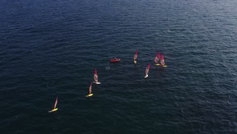 Group-of-windsurfers-with-yellow-and-white-surfboards-gathered-around-an-orange-speedboat-in-the-Mediterranean-Sea-near-Herzeliya