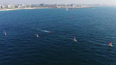 Mehrere-Windsurfer-Surfen-Mit-Hoher-Geschwindigkeit-über-Das-Wunderschöne-Blaue-Wasser-Des-Mittelmeers-Mit-Der-Stadt-Herzeliya-Im-Hintergrund