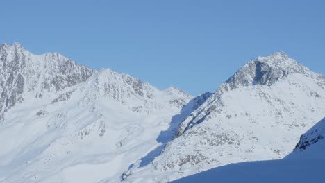 Snowy-peaks-and-ridges,-bright,-sunny-winter-day-with-blue-sky-in-the-Alps---pan-view