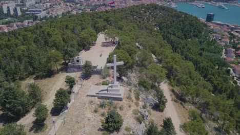Flying-around-the-white-stone-cross,-keeping-it-as-the-main-subject-with-the-port-and-city-of-Split-in-the-background
