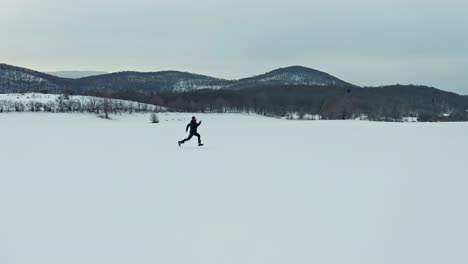 Aerial-drone-shot-of-the-man-running-in-the-snow