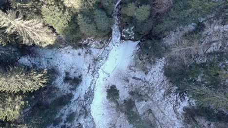 Drohne-Steigt-Auf-Schneebedeckten-Waldbergen-Mit-Eisigem-Fluss-Auf