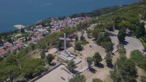 Flying-away-from-the-white-stone-cross-of-Park-Suma-Marjan,-Split,-Croatia,-with-the-Adriatic-Sea-in-the-background