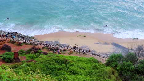 Playa-De-Mar-Con-Agua-Azul-Rompiendo-Olas-Y-Un-Entorno-Verde-Desde-El-ángulo-Superior-Video-Tomado-En-Verkala-Beach-Kerala-India