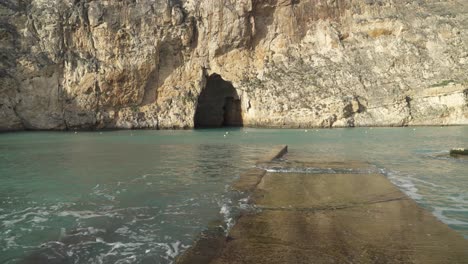 Gehen-Sie-Auf-Einem-Steinpier-In-Richtung-Binnenseehöhlen-Mit-Klippen,-Die-Das-Mittelmeer-Waschen