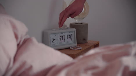 Hand-is-changing-white-Retro-Flip-Clock-Calendar-Date-and-Day-next-to-the-bed-in-the-morning