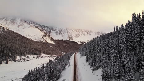 Drohnen-Luftaufnahmen-Fliegen-über-Eine-Einsame-Bergstraße-Im-Rocky-Mountains-Tal,-Umgeben-Von-Schnee-Und-Kiefern,-Während-Des-Wunderschönen-Goldenen-Sonnenuntergangs-In-Loveland-Pass,-Colorado