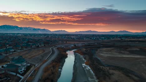 Brilliantly-colorful-sunrise-above-the-snowy-mountain-community-and-reflecting-off-the-surface-of-the-river---aerial-hyper-lapse
