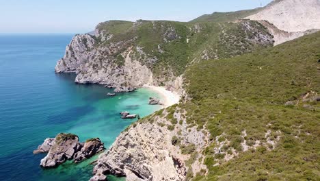 Aerial-Drone-View-of-Ribeira-do-Cavalo-Beach-at-Sesimbra,-Portugal---Flying-Over-the-Coastline-with-Rocky-Green-Mountains,-Blue-Atlantic-Ocean-and-Hidden-Sandy-Beach