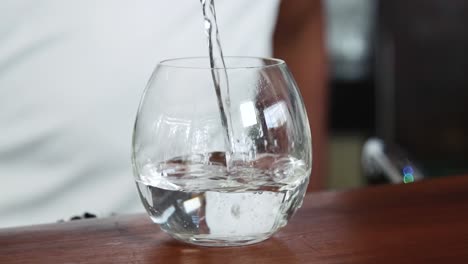 Pouring-water-in-a-round-shaped-glass,-serving-water-in-a-transparent-and-crystal-glass