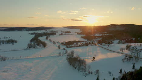 Picturesque-winter-aerial-flying-over-a-frozen,-snow-covered-landscape-at-sunset