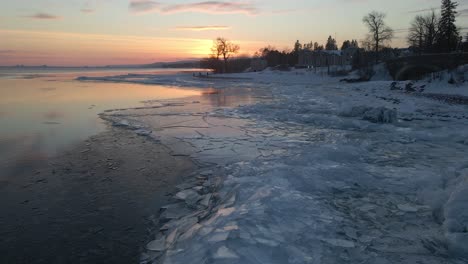 Triangle-ice-formations-pilled-up-on-the-Shores-of-Lake-superior,-water-reflections-during-a-winter-sunset