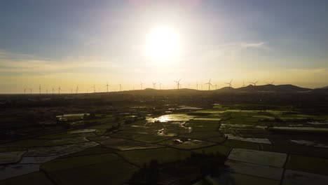 Blick-Auf-Den-Sonnenuntergang-Aus-Der-Luft-Auf-Landwirtschaftlichen-Reisfeldern-In-Der-Nachbarschaft-Von-Lien-Huong-Mit-Einer-Windmühlenturbine,-Die-Am-Horizont-Bis-Zu-Den-Hügeln-Der-Vietnamesischen-Ländlichen-Landschaft-Aufgereiht-Ist