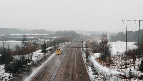 Aerial-shot-of-a-speed-train,-Arlanda-Express-passing-by-under-drone-in-industrial,-winter-landscape-going-towards-Arlanda-Airport