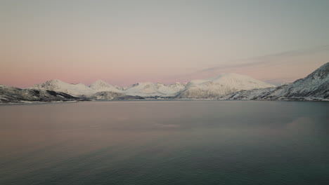 Pink-Sunset-Over-Fjord-With-Snowy-Mountains-In-Background,-Kvaloya,-Norway---aerial-drone-shot