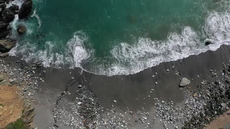 Top-Down-View-Of-Waves-Splashing-On-Rocky-Shore---aerial-drone-shot