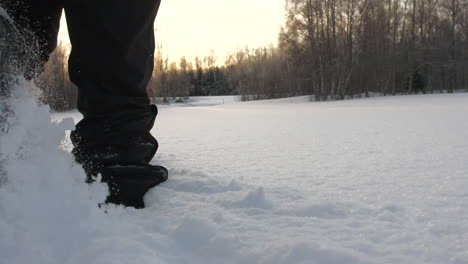 Person-walking-through-deep-pure-white-snow-in-forestry-area,-low-angle-close-up-back-shot