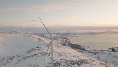 Windkraftanlagen-Auf-Schneebedeckten-Arktischen-Bergen-Mit-Blick-Auf-Den-Fjord
