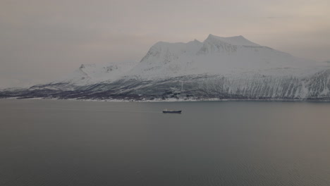 Barco-De-Carga-Navegando-En-El-Fiordo-Con-Montañas-Nevadas-En-El-Fondo-En-Kvaloya,-Tromso,-Noruega