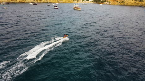 Paar-Jetskiing-Im-Blauen-Ozean-Vorbei-An-Verankerten-Booten-Auf-Der-Insel-Ibiza,-Spanien