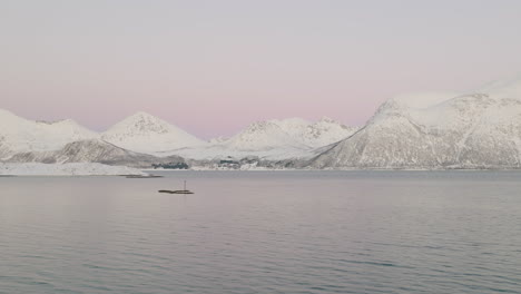 Volando-Sobre-Un-Mar-En-Calma-Con-La-Isla-Montañosa-De-Kvaloya-Cubierta-De-Nieve-En-Invierno-En-El-Norte-De-Noruega