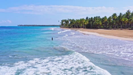Aerial-drone-view-passing-a-man-fishing-in-waves,-at-the-Playa-Coson-beach,-in-Dominican-republic