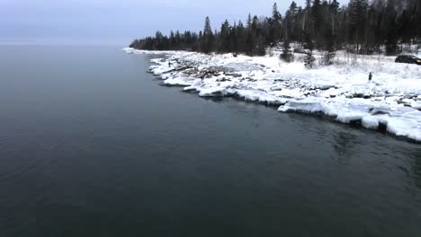Aerial-view-of-Lake-Superior-on-a-winter-cloudy-afternoon,-forest-by-the-shore