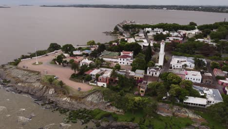 Aerial-orbit-shot-of-lighthouse-and-shoreline-of-Colonia-del-Sacramento-City-in-Uruguay-during-dark-cloudy-day