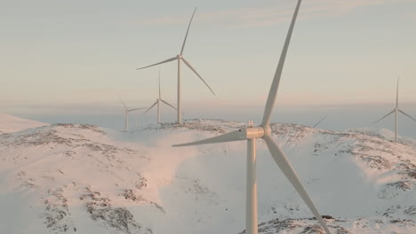 Close-up-drone-view-of-spinning-wind-turbine-on-snowy-mountain