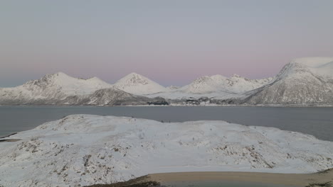Drone-pullback-reveals-snowy-island-in-fjord-with-stark-white-mountains