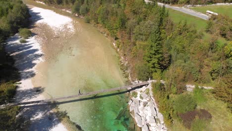 aerial-side-view-of-man-walking-across-rope-bridge-over-Soca-river-in-Slovenia