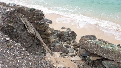 Ocean-sea-wall-and-road-corrosion,-collapsed-due-to-impacts-of-rising-tides,-climate-change,-with-waves-gentle-washing-onto-the-beach