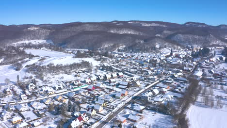 Charming-Town-At-The-Foot-Of-The-Mountains-Covered-In-Thick-Snow-In-Winter---aerial-shot