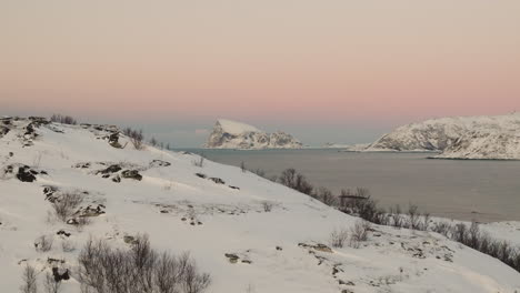 Snow-covered-Haaja-Island-on-horizon-over-fiord,-pink-sunset-sky
