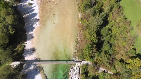 aerial-top-down-view-of-rope-bridge-over-beautiful-emerald-river,-man-walking-across