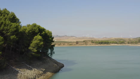 Wind-turbines-beyond-an-island-with-trees,-lake-Caminito-del-Rey,Spain