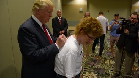 Donald-Trump-Firma-Una-Camiseta-De-Mujer-Conservadora-Y-Habla-Con-Una-Joven-Simpatizante-En-Un-Mitin,-Iowa-Caucus