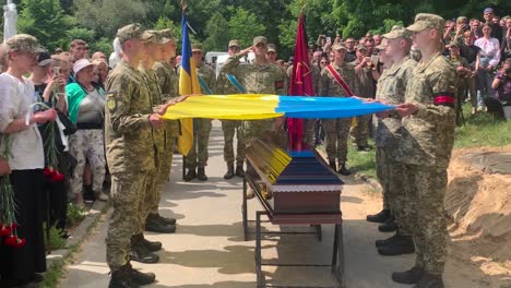 Eine-Ukrainische-Flagge-Wird-Während-Einer-Militärischen-Beerdigung-Infolge-Des-Ukrainekriegs-Auf-Den-Sarg-Eines-Soldaten-Gelegt-Und-Es-Wird-Ein-Salutschuss-Mit-21-Schüssen-Abgehalten