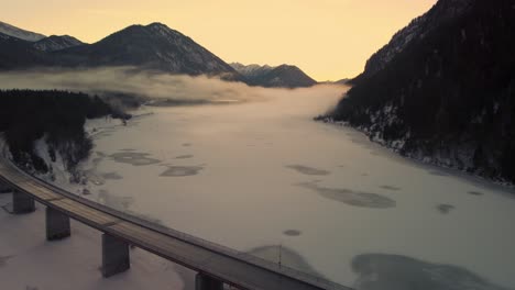 Puente-De-Depósito-De-Agua-Potable-De-Sylvenstein-En-Los-Hermosos-Alpes-Austríacos-Bávaros-En-Invierno-Nevado-Con-Montañas-Y-Agua-Azul-Clara-Al-Atardecer