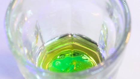 Macro-shot-of-green-substance-falling-into-golden-liquid