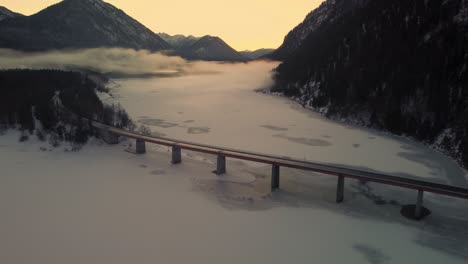 Sylvenstein-Speicher-fresh-drinking-water-Sylvenstein-reservoir-bridge-in-the-scenic-Bavarian-Austrian-alps-in-snow-winter-with-mountains-and-clear-blue-water-by-sunset