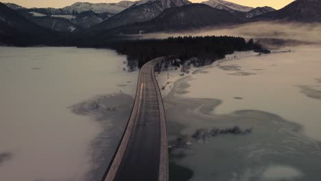 Sylvenstein-fresh-drinking-water-reservoir-bridge-in-the-scenic-Bavarian-Austrian-alps-in-snow-winter-with-mountains-and-clear-blue-water-by-sunset