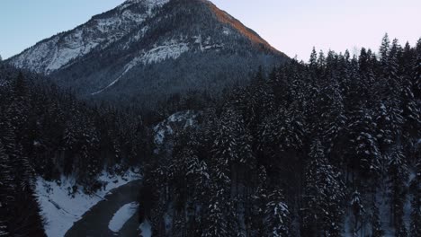 Flying-toward-a-huge-and-impressive-mountain-with-forest-and-trees-in-winter-with-snow-and-ice-in-the-idyllic-and-scenic-Bavarian-Austrian-alps-mountains-with-red-sunset-peaks