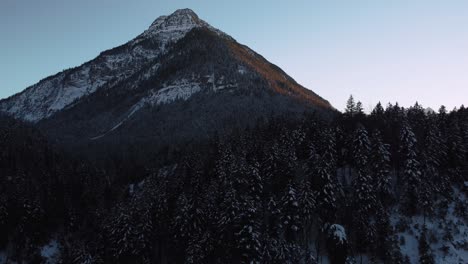 Rundflug-Zu-Einem-Riesigen-Und-Beeindruckenden-Berg-Mit-Wald-Und-Bäumen-Im-Winter-Mit-Schnee-Und-Eis-In-Den-Idyllischen-Bayerischen-österreichischen-Alpenbergen-Mit-Roten-Sonnenuntergangsgipfeln