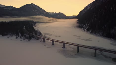 Sylvensteinspeicher-fresh-drinking-water-Sylvenstein-reservoir-bridge-in-the-idyllic-Bavarian-Austrian-alps-in-snow-winter-with-mountains-and-clear-blue-water-by-sunset