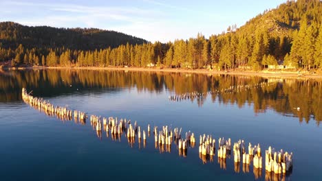 Evening-Sunset-Drone-Aerial-Over-Glenbrook,-Lake-Tahoe,-Nevada,-With-Old-Pier-Pilings-Coming-Out-Of-Calm-Water