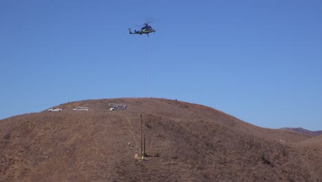 Ein-Schwebender-Hubschrauber-Hilft-Beim-Austausch-Von-Telefonmasten-Für-Ein-Elektroarbeiterteam-Auf-Einem-Kalifornischen-Hügel