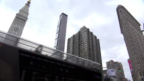 Bus-Mit-Niedrigem-Winkel,-Der-Mit-Flatiron-Und-Anderen-Manhattan-New-York-Gebäuden-Im-Hintergrund-Vorbeifährt