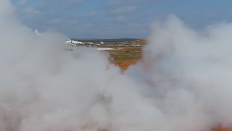 Aerial-Past-Steaming-Hot-Fumeroles-In-A-Geothermal-Aera-Reveals-A-Geothermal-Power-Plant-In-The-Distance